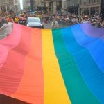 Participants carrying a large rainbow flag down the street during the 2024 NYC Pride Parade.
