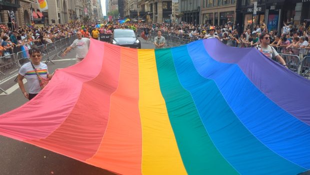 Participants carrying a large rainbow flag down the street during the 2024 NYC Pride Parade.